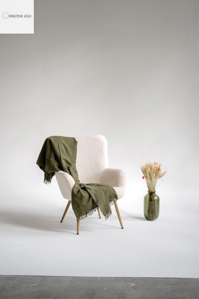 a chair with a blanket on it next to a vase with flowers